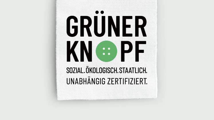 Logo: schwarze Schrift auf einem weißen Stoffetikett. Das „O“ des Worts „Knopf“ ist als grüner Knopf gestaltet