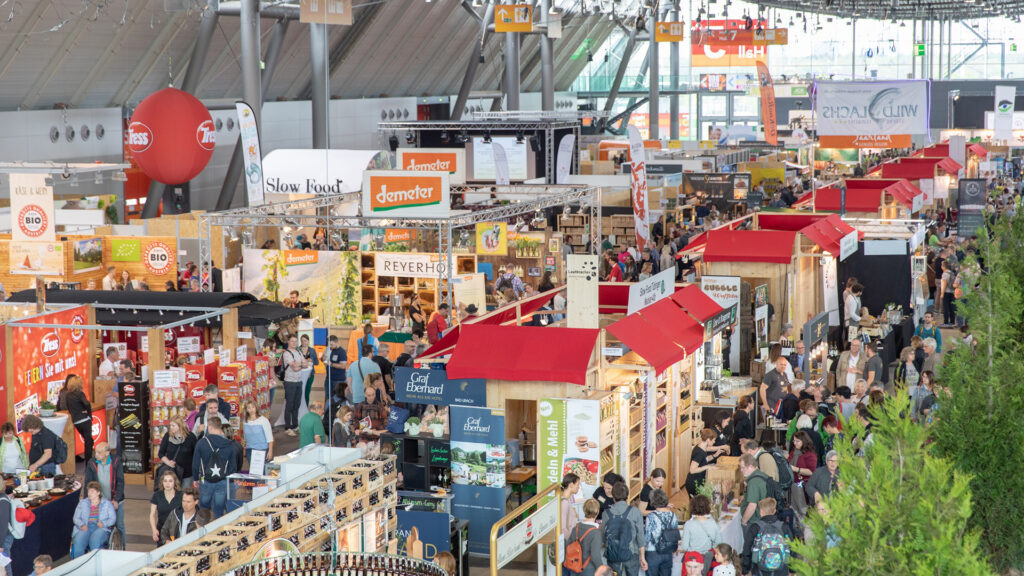 Bild: Blick von oben in eine Messehalle mit vielen kleinen Messeständen und dazwischen zahlreiche Besucher