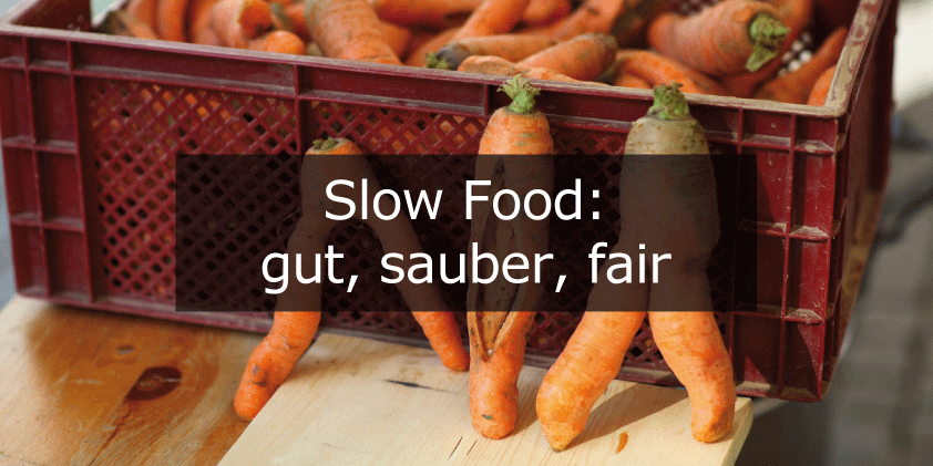 Bild: eine rote Kiste mit organgefarbenen Karotten und davor der Schriftzug „Slow Food: gut, sauber, fair“ in weiß auf schwarzem, halbtranparentem Untergrund